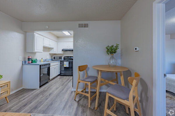 Open-plan kitchen with white cabinets, black appliances, and a round wooden dining table with chairs in a small dining nook.