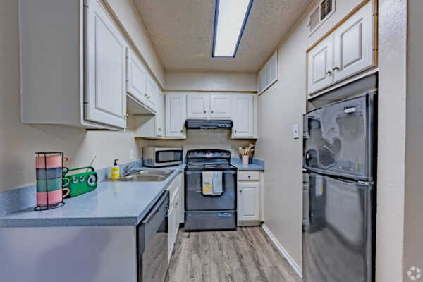 Narrow galley kitchen with white cabinets, blue speckled countertops, and stainless steel appliances along a long walkway.