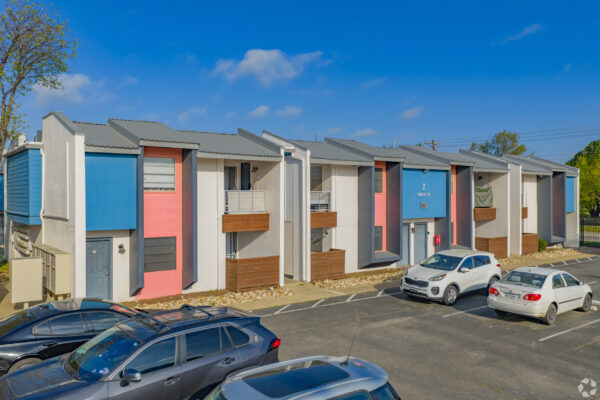 Row of colorful modern townhouses under a clear blue sky with parked cars along the street.